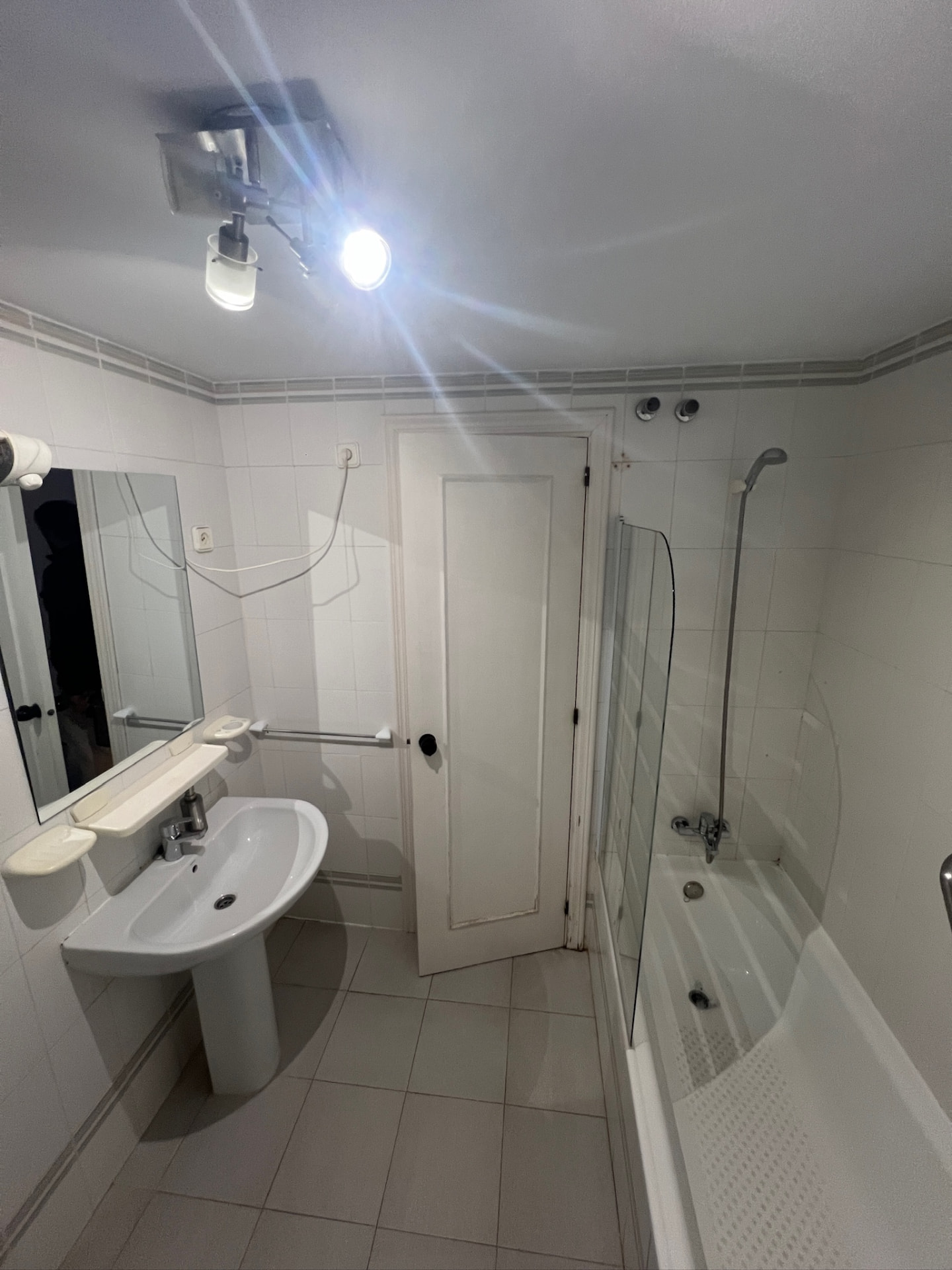 The bathroom before: the bathtub with a curved glass splash screen and a handheld shower rail