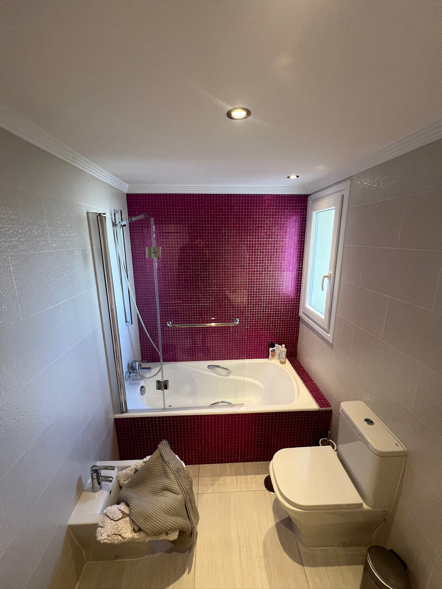The bathroom before: a bathtub set into a wall of glossy red mosaic tiles