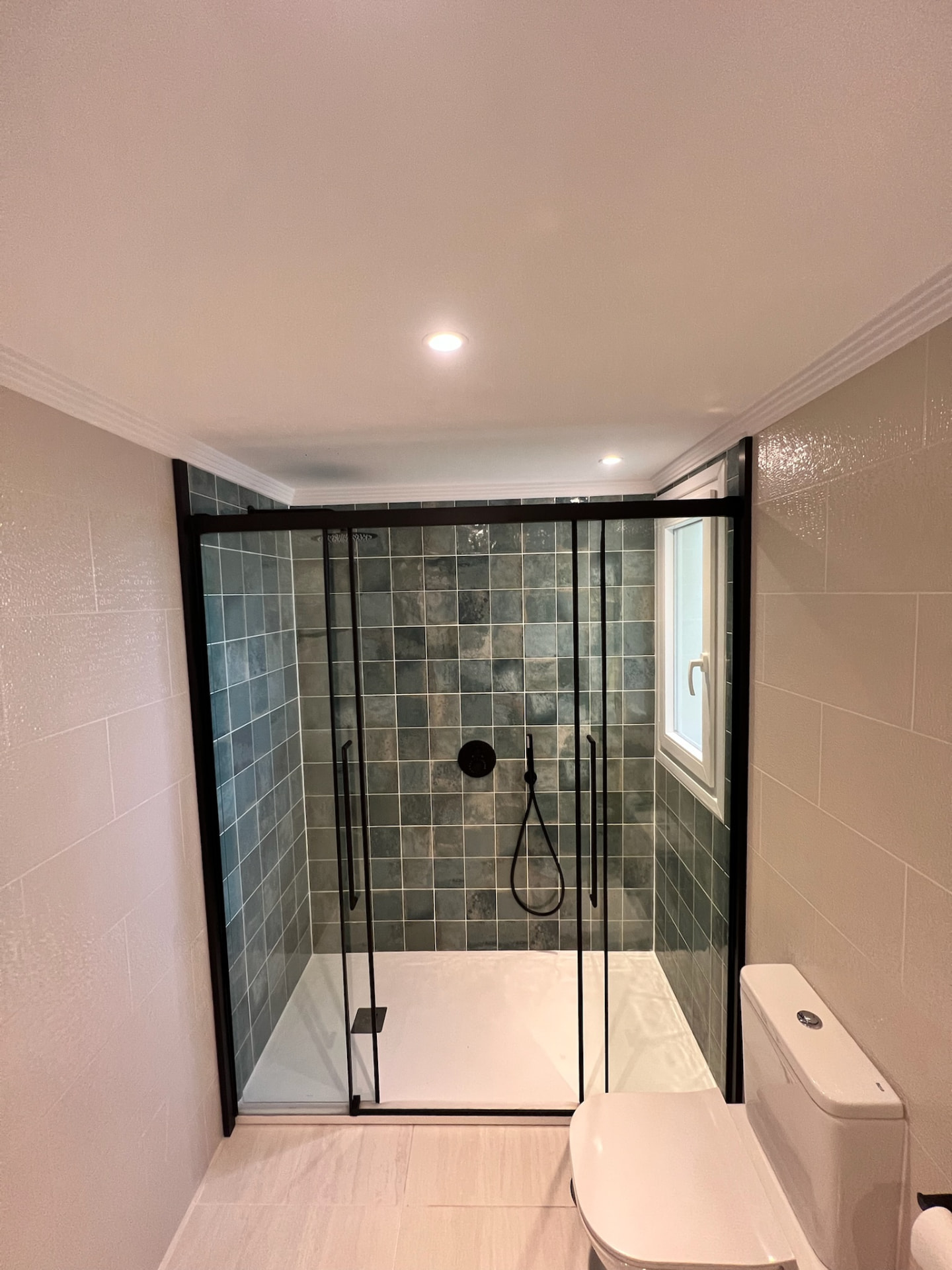 The same bathroom after: a walk-in shower with a matte black frame and green tiles