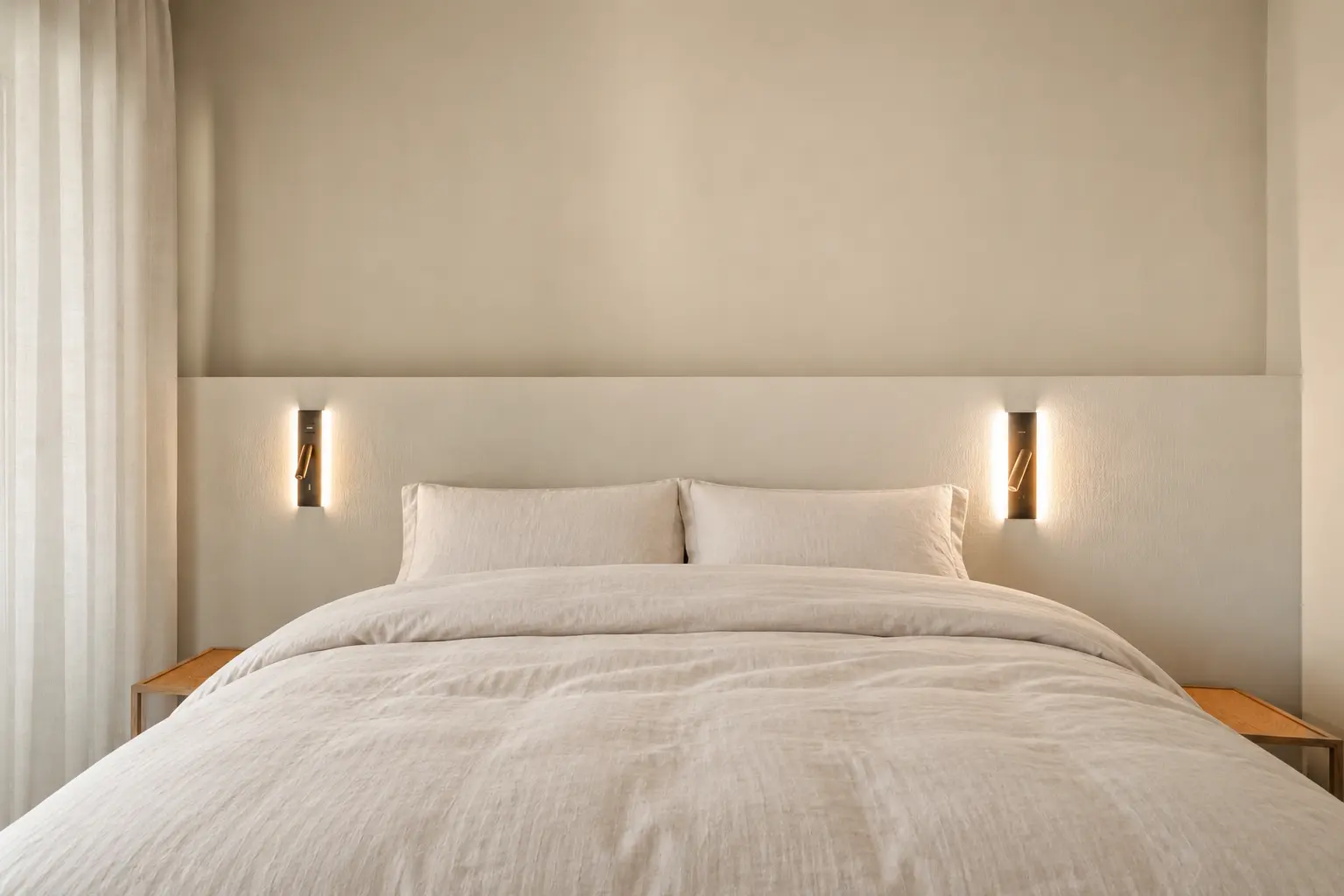 The bedroom: a linen bed between oak nightstands, with wall lights either side of the headboard