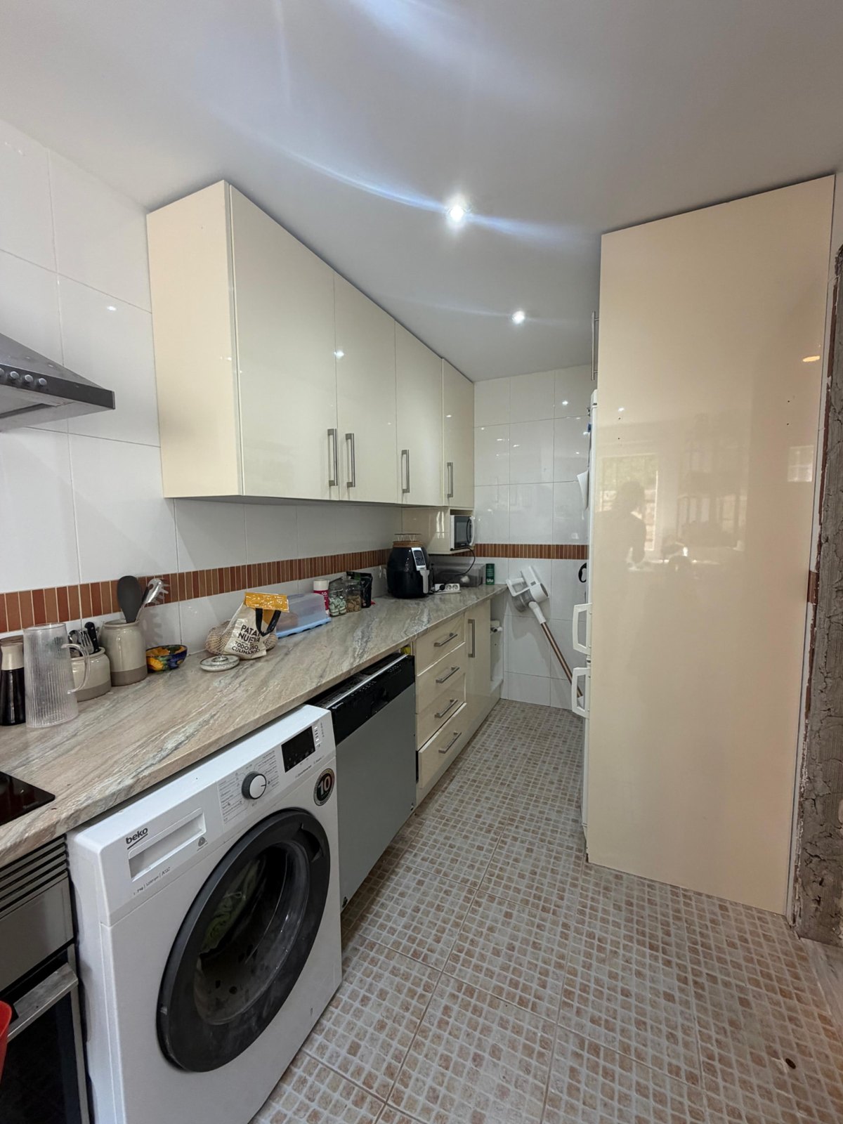 Kitchen in Alhaurín el Grande before: glossy wall units, a washing machine under the worktop and a tall fridge
