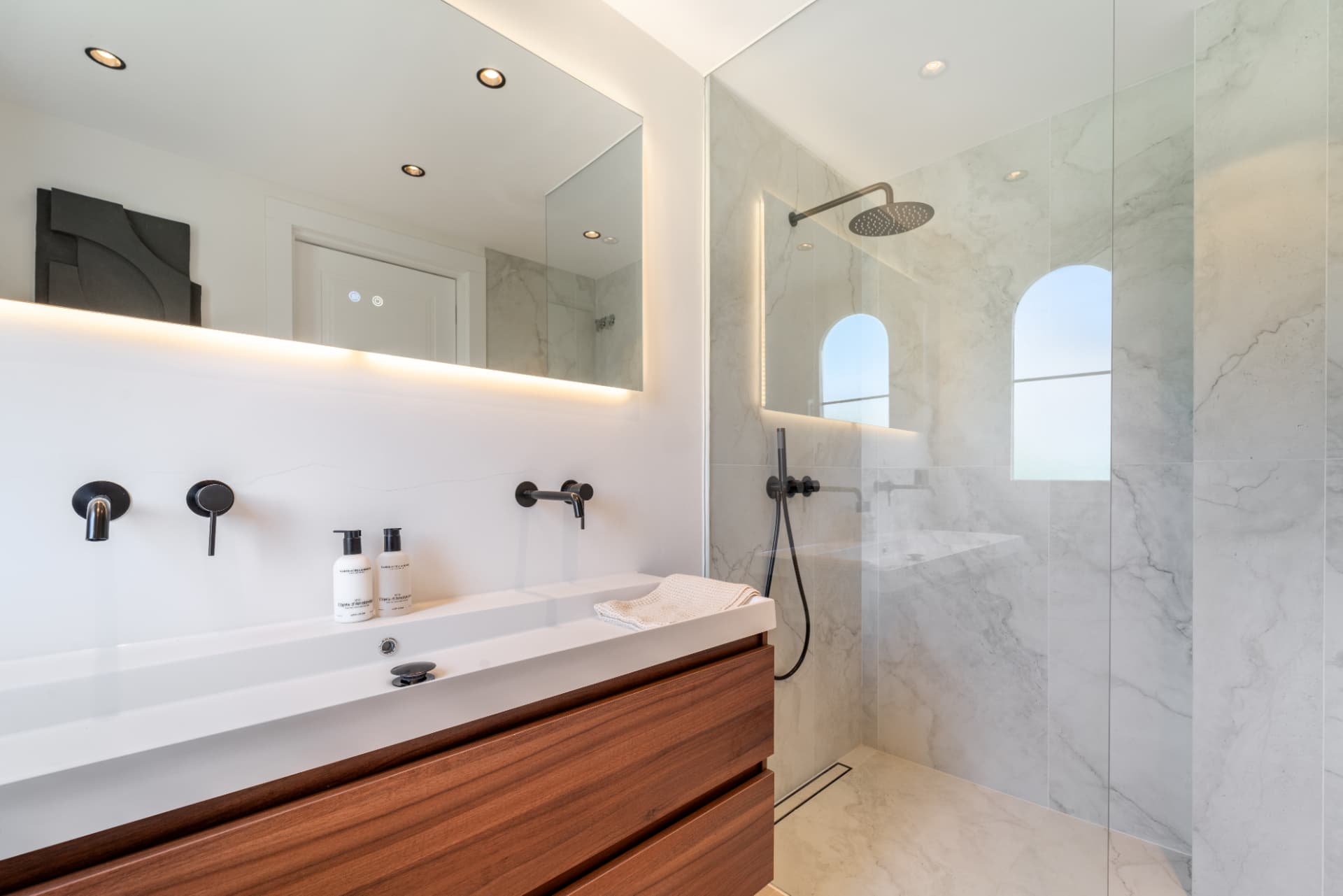 Bathroom with walk-in shower, wooden vanity and backlit mirror