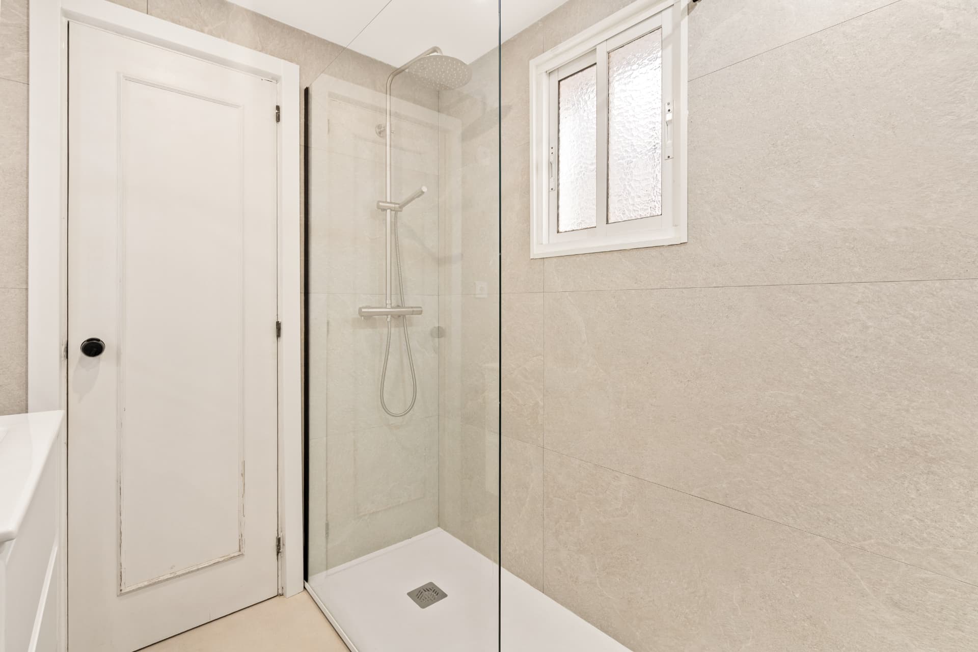 The bathroom after: the walk-in shower with a frameless glass screen and a rain shower column