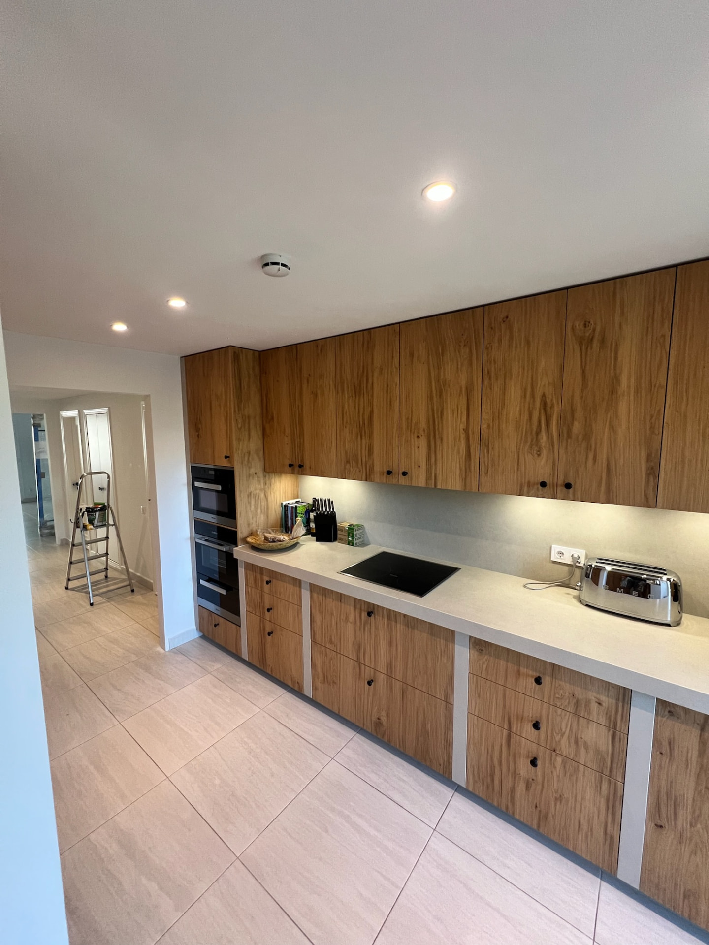 The kitchen after: full-height wood cabinets, light stone worktop and a flush black cooktop