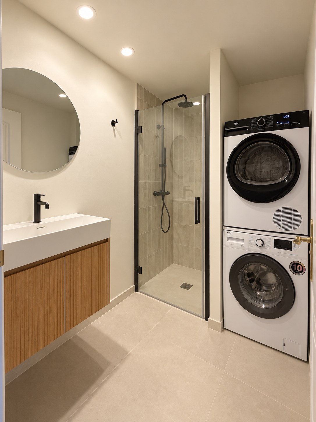 The bathroom after: an oak vanity with an integrated basin, a round mirror, a walk-in shower with black fittings and a stacked washer and dryer